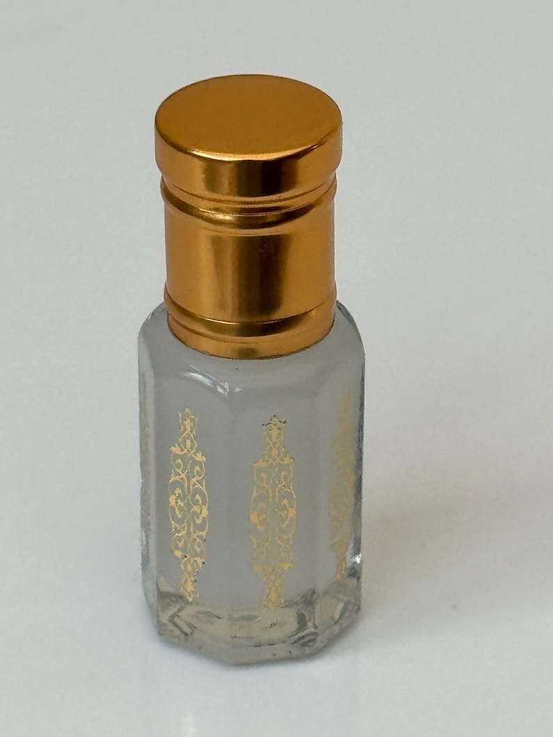 Pode incluir: Frasco de perfume pequeno, de vidro transparente, com tampa dourada. O frasco tem padr&otilde;es decorativos dourados na frente. Projetado para conter perfume ou &oacute;leos essenciais.