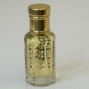 May include: A small, clear glass bottle with a gold cap and intricate gold designs on the bottle. The bottle is filled with a light yellow liquid.