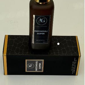 May include: A brown perfume bottle with a gold cap sits atop a black box. The bottle has a label that reads "PATCHOULI SUPER" and the box has a repeating pattern. The perfume bottle is rectangular and the box is rectangular.