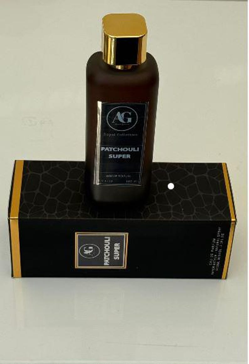 May include: A brown perfume bottle with a gold cap sits atop a black box. The bottle has a label that reads "PATCHOULI SUPER" and the box has a repeating pattern. The perfume bottle is rectangular and the box is rectangular.