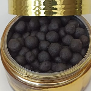 May include: A gold jar with a lid filled with dark brown round incense pellets.