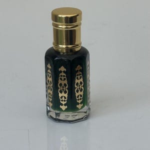 May include: A small, clear glass bottle with a gold cap. The bottle is filled with a dark green liquid and has gold decorative designs on the front.