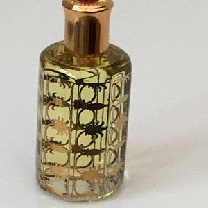 May include: A small, clear glass bottle with a gold cap and a red top. The bottle is filled with a light yellow liquid and has a gold patterned design.