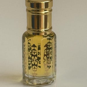 May include: A small, clear glass bottle with a gold cap and intricate gold designs. The bottle is filled with a light yellow liquid.