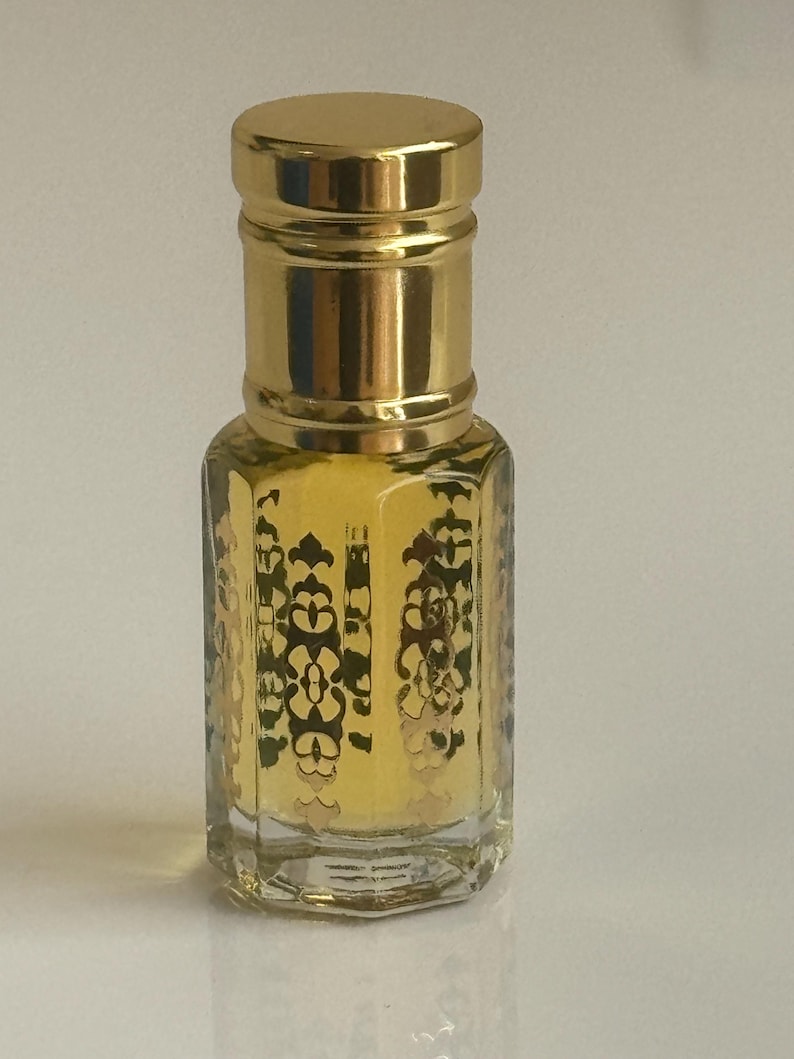 May include: A small, clear glass bottle with a gold cap and intricate gold designs. The bottle is filled with a light yellow liquid.