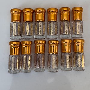 Könnte beinhalten: Ein Set aus zwölf kleinen Parfümflakons aus klarem Glas, angeordnet in zwei Reihen zu je sechs Stück. Jeder Flakon verfügt über einen goldenen Schraubverschluss aus Metall und aufgedruckte goldfarbene Verzierungen auf der Vorderseite.