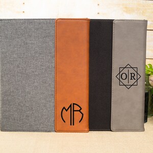 May include: Three different styles of personalized leatherette document folders. The first folder is gray with a gray fabric cover. The second folder is brown with a monogram "MR" in a circle. The third folder is gray with a black monogram "OR" in a geometric design.