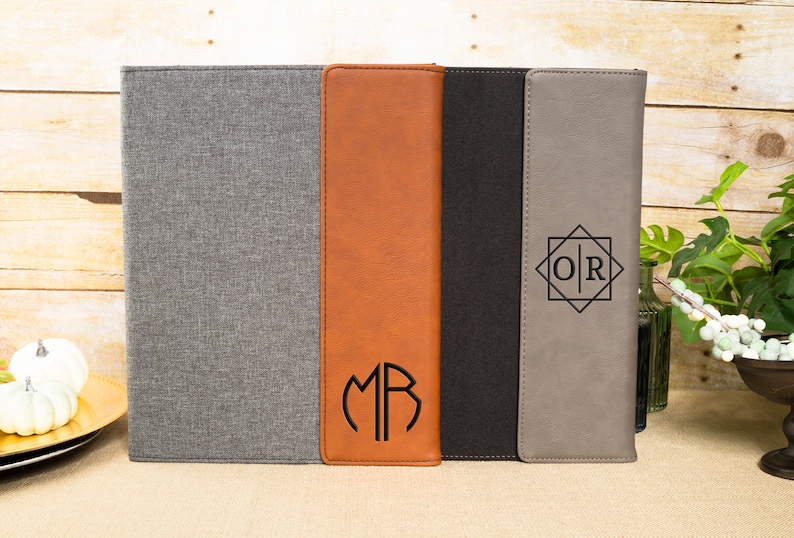May include: Three different styles of personalized leatherette document folders. The first folder is gray with a gray fabric cover. The second folder is brown with a monogram "MR" in a circle. The third folder is gray with a black monogram "OR" in a geometric design.