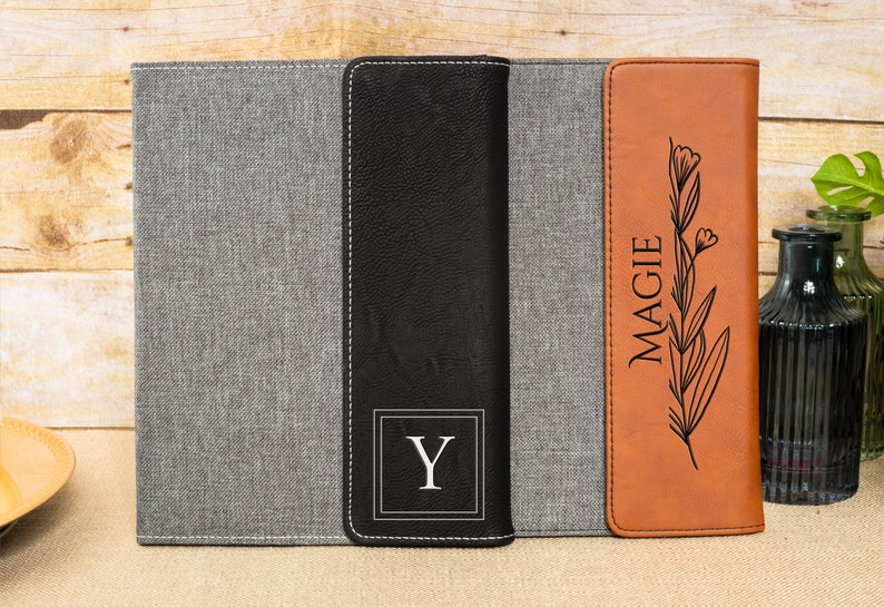 May include: A set of three personalized leatherette journals with a gray, black, and brown cover. The covers are embossed with a floral design and the name "MAGGIE" and the initial "Y".