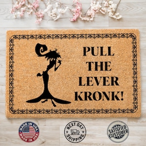 May include: A rectangular doormat made of natural coir fiber. The mat features a black silhouette of a character and the text "PULL THE LEVER KRONK!". The border is a decorative black pattern.