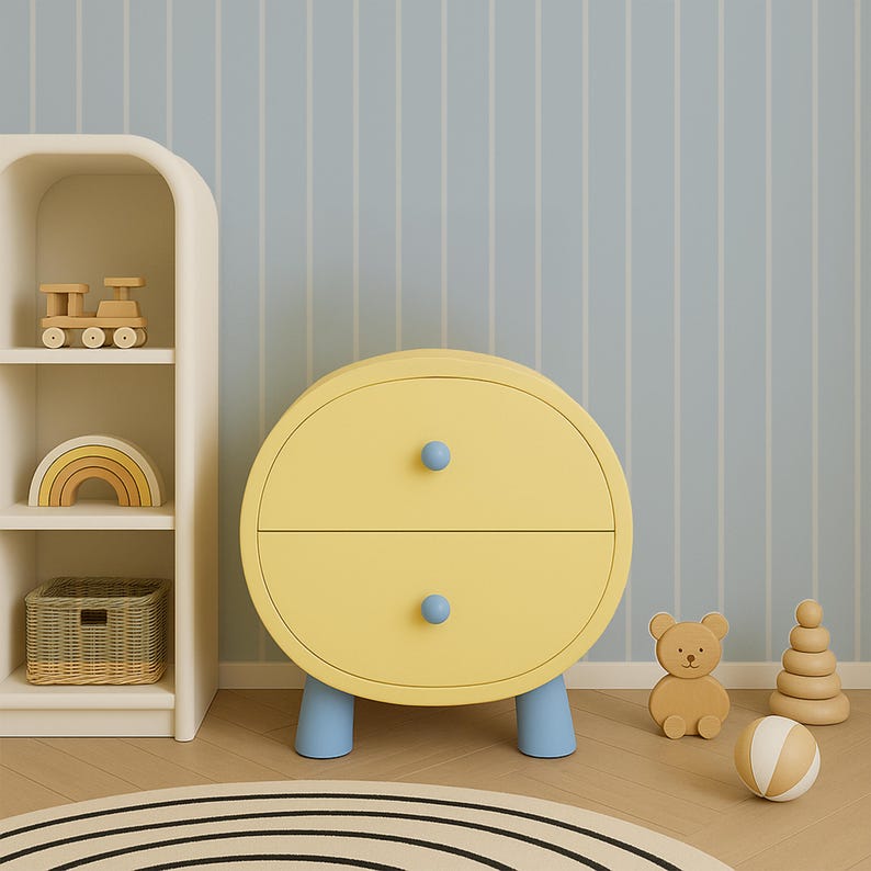 May include: A yellow, round two-drawer nightstand with blue legs and knobs. A white shelf unit holds a wooden train, rainbow, and basket. A wooden bear, stacking rings, and ball sit on the floor. The room has a striped blue and white wallpaper.