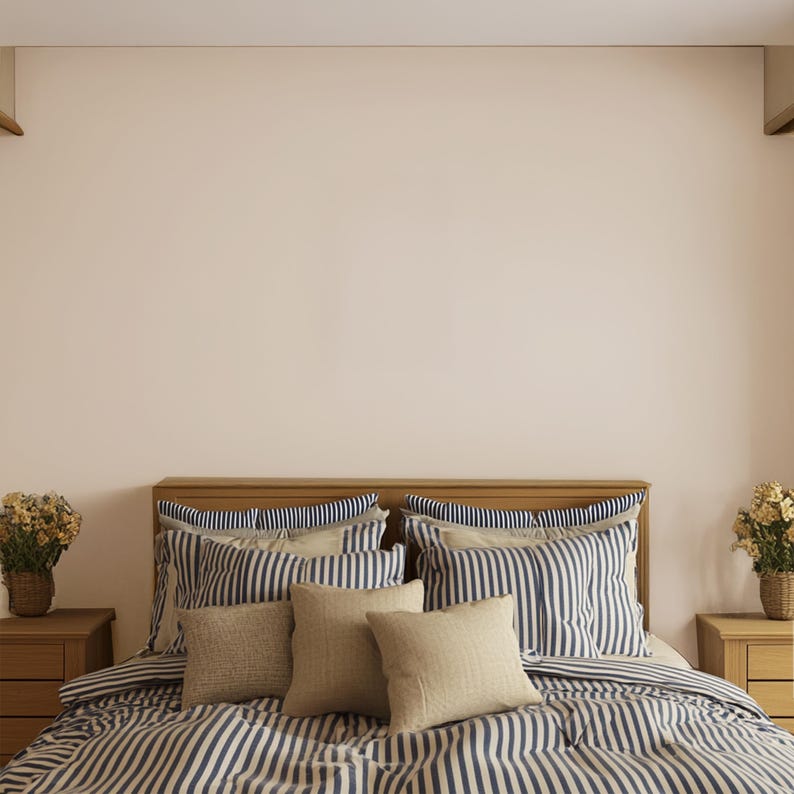 May include: A bed with a wooden headboard and matching nightstands. The bedding features a blue and white striped pattern, with several pillows in matching stripes and solid beige. Two small flower arrangements sit on the nightstands.