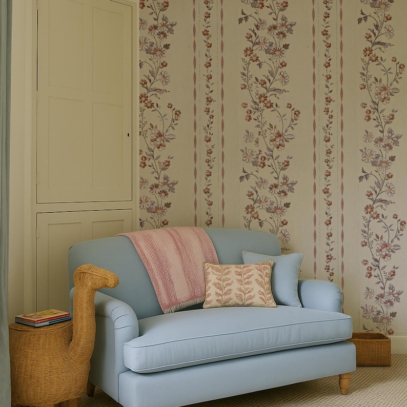 May include: A light blue sofa with a pink and white striped throw blanket and a decorative pillow with a leaf pattern. The sofa is in front of floral wallpaper. A woven side table with a book and a decorative giraffe is to the left.