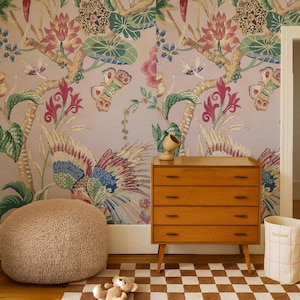May include: A room scene featuring a wooden dresser with four drawers, a plush round ottoman, and a checkered rug. The wall is adorned with a colorful floral and butterfly wallpaper. A teddy bear and a woven basket complete the decor.