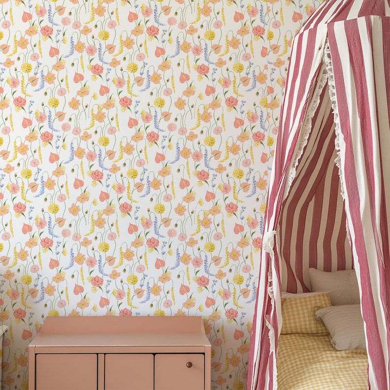 May include: A bedroom scene featuring floral wallpaper with pink, yellow, and blue flowers on a white background. A pink dresser is in the foreground, and a striped canopy bed with pillows and a yellow gingham blanket is on the right.