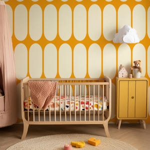 May include: A nursery scene featuring a light wood crib with a patterned sheet and a peach-colored blanket. A yellow cabinet with a teddy bear and decorative items sits beside the crib. The background is a yellow and cream oval pattern.