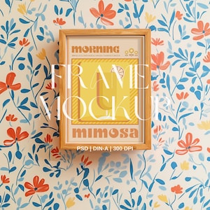 May include: A wooden frame mockup with a floral background. The frame has a white mount and a clear glass front. The image inside the frame is a digital illustration of a mimosa cocktail with the text "morning" and "mimosa".