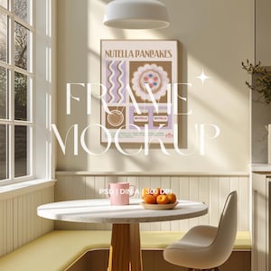 May include: A framed poster with the text "NUTELLA PANCAKES" hangs above a round table. The poster features illustrations of pancakes and Nutella jars. A pink mug and a plate of oranges sit on the table. A modern chair is next to the table.