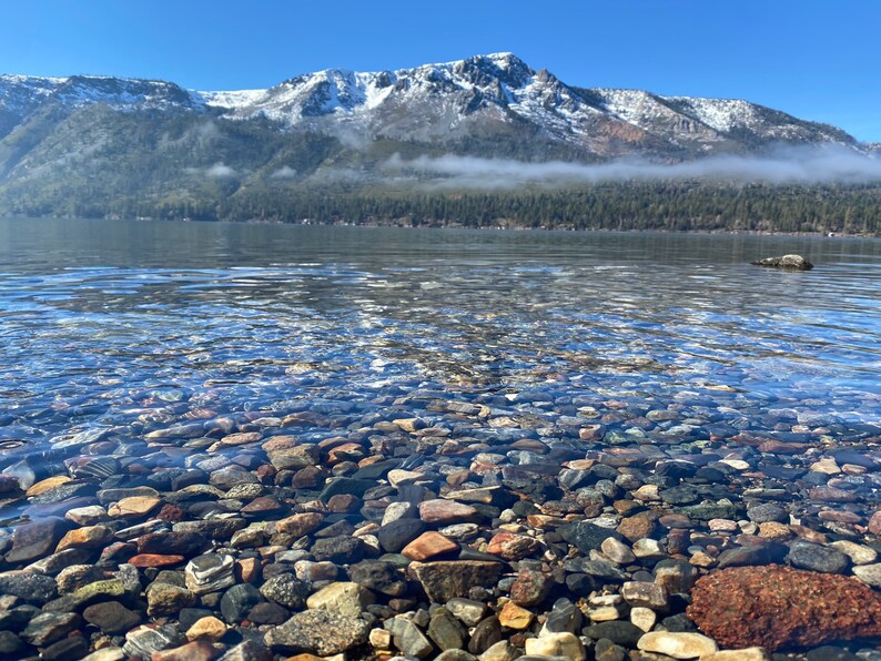 Pode incluir: Um lago de montanha claro com um fundo rochoso e uma cordilheira nevada ao fundo.