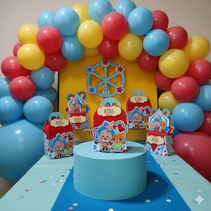 Op de afbeelding: Een feestelijke scène met een ballonnenboog in blauw, rood en geel. De scène omvat een blauwe cilindrische standaard met geschenkdozen en een achtergrond met een reuzenraddesign. De geschenkdozen dragen de naam "AZIEL".