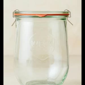 May include: A clear glass preserving jar with a hinged lid and an orange rubber seal. The jar has a wide mouth and a rounded body. The word "WECK" is embossed on the front. Ideal for preserving food, it is made of glass.