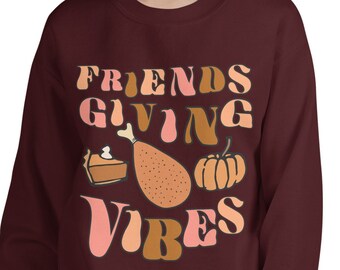 Könnte beinhalten: Ein weinrotes Sweatshirt mit dem Schriftzug "FRIENDS GIVING VIBES" in einem Retro-Schriftstil. Das Design umfasst Illustrationen eines Kuchenstücks, einer Truthahnkeule und eines Kürbisses. Das Sweatshirt ist ein bequemer, lässiger Stil.