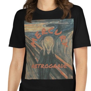 May include: Black t-shirt with a graphic print of a painting of a person screaming. The painting is in a style similar to Edvard Munch's "The Scream". The text "Mercury Retrograde" is printed in red on the shirt.