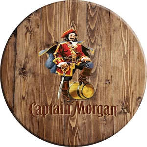 May include: A round wooden sign with a brown wood grain pattern. The sign features a cartoon image of Captain Morgan, a pirate, standing on a barrel. The text "Captain Morgan" is printed in brown letters on the sign.