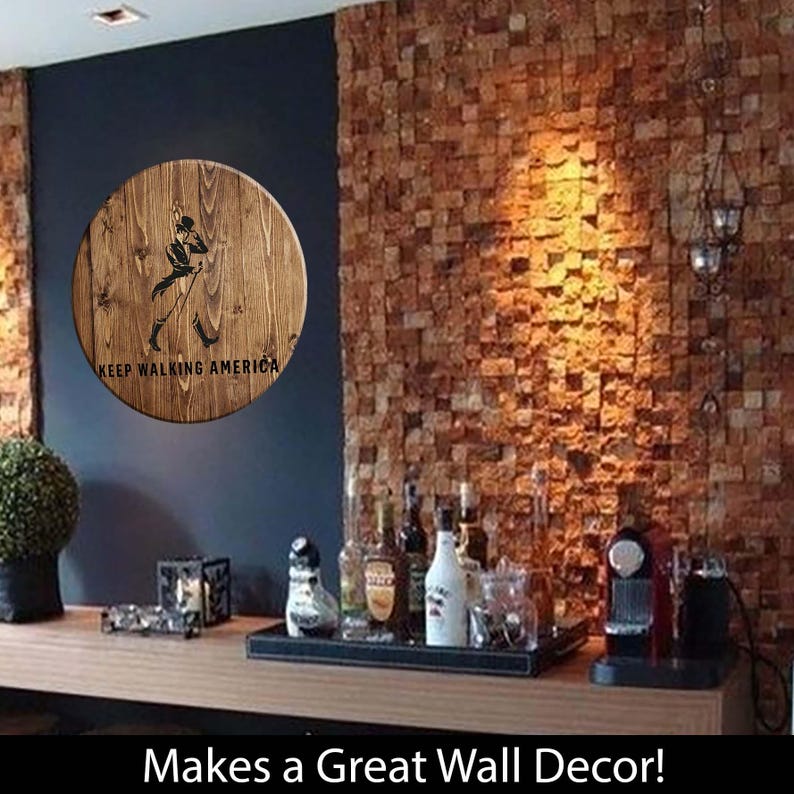 Puede incluir: Un letrero redondo de madera con la silueta de una persona caminando y el texto "Keep Walking America". El letrero est&aacute; montado en una pared de ladrillo en un ambiente de bar.