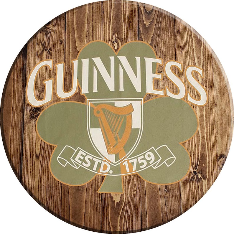 May include: A round wooden sign with a brown wood grain background. The sign features a green shamrock with a white harp inside. The words "GUINNESS ESTD. 1759" are printed on the sign.