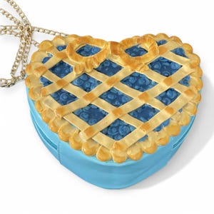 May include: A blue heart-shaped purse with a gold chain strap. The purse is designed to look like a blueberry pie with a lattice crust.