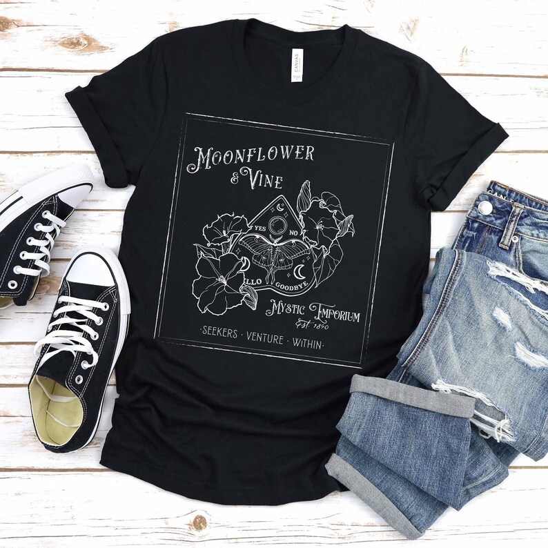 Pode incluir: Camiseta preta com um design gr&aacute;fico branco de uma flor de lua e uma videira com um tabuleiro Ouija e o texto "Moonflower & Vine Mystic Emporium est 1890 - Seekers Venture Within - "