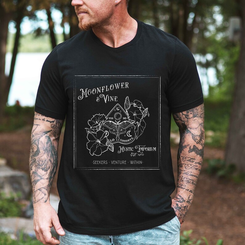 Pode incluir: Camiseta preta com um design gr&aacute;fico branco que apresenta uma flor de lua e uma videira, um s&iacute;mbolo m&iacute;stico, e o texto "Moonflower & Vine Mystic Emporium est. 2020 Seekers - Venture - Within."