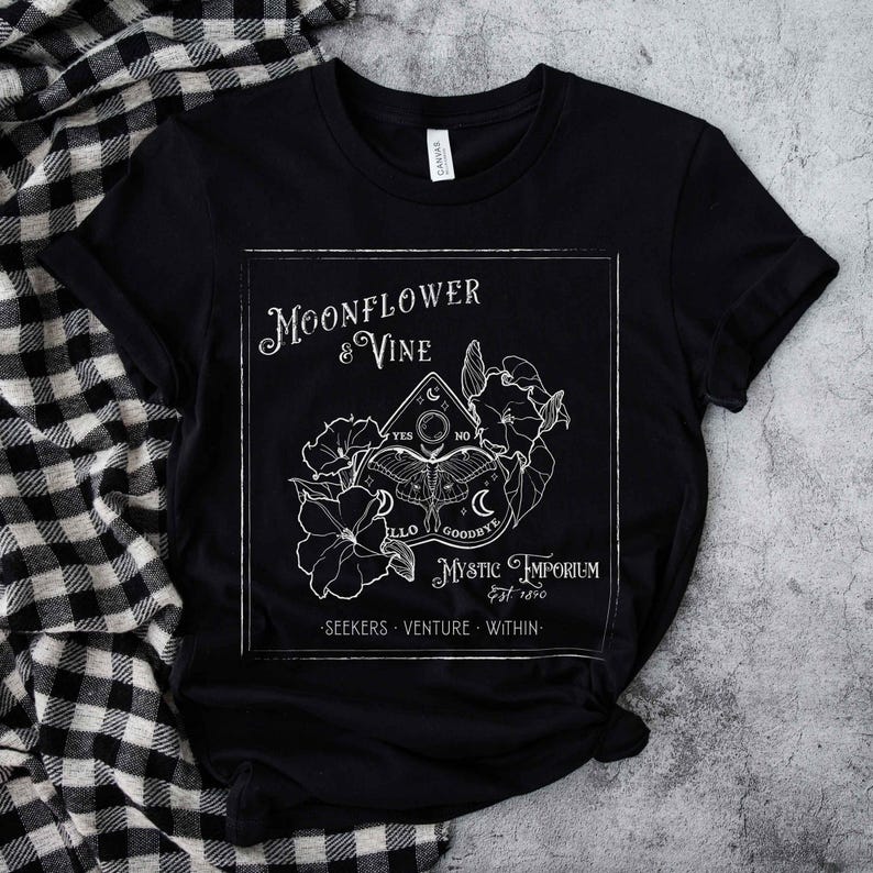 Pode incluir: Camiseta preta com um design gr&aacute;fico branco de uma flor de lua e uma videira com um tabuleiro Ouija e o texto "Moonflower & Vine Mystic Emporium Est 1890 Seekers Venture Within"