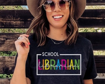 May include: A dark grey t-shirt with the text "SCHOOL LIBRARIAN" in a white box with a rainbow colored border.
