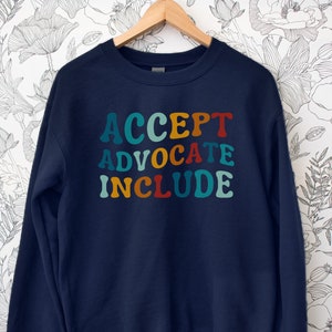 May include: Navy blue sweatshirt with the words "ACCEPT ADVOCATE INCLUDE" in colourful retro lettering.