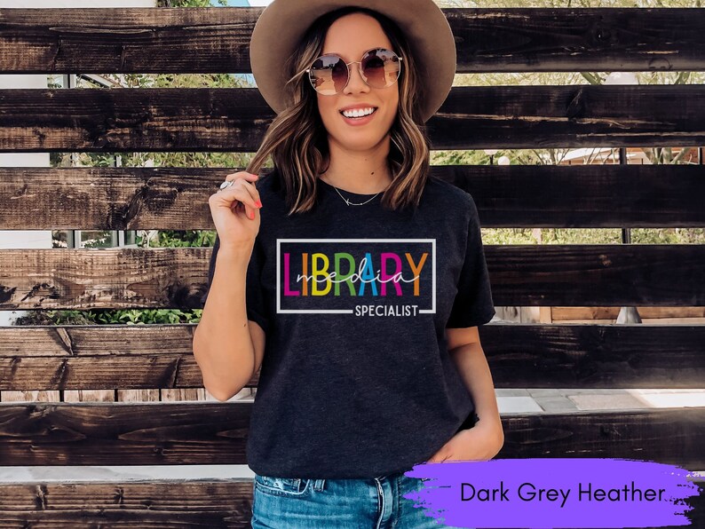May include: Dark grey heather t-shirt with the text "LIBRARY SPECIALIST" in a colorful rainbow font.