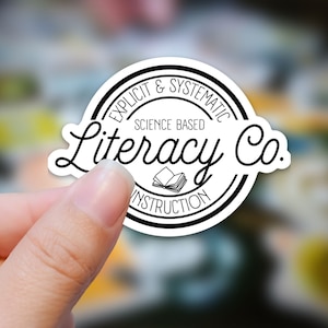 May include: Black and white sticker with the text "Explicit & Systematic Science Based Literacy Co." in a circle with a stack of books inside.