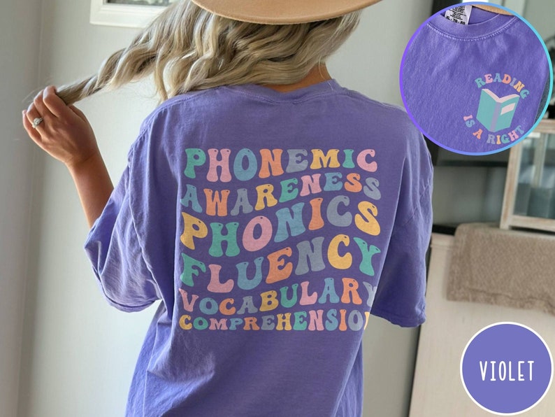 May include: A purple t-shirt with the words "phonemic awareness, phonics, fluency, vocabulary, comprehension" in rainbow colors on the back. The front of the shirt has a small graphic of a book with the text "Reading is a right" in a light blue color.