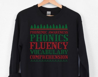 Może przedstawiać: Czarna bluza z świątecznym wzorem z napisami "Phonemic Awareness, Phonics, Fluency, Vocabulary, Comprehension" w kolorze czerwonym i zielonym.