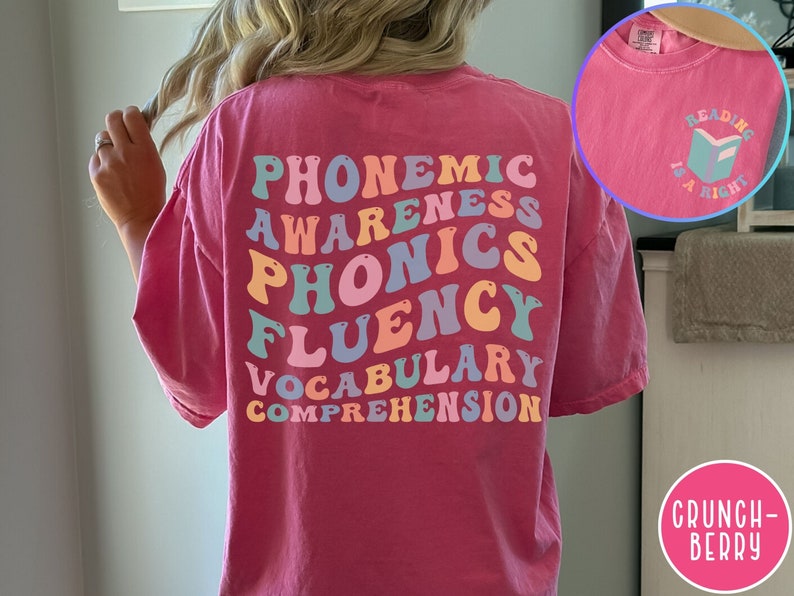 May include: Pink t-shirt with the words "phonemic awareness, phonics, fluency, vocabulary, comprehension" in rainbow colors on the back. The front of the shirt has a small book icon with the text "Reading is a right".