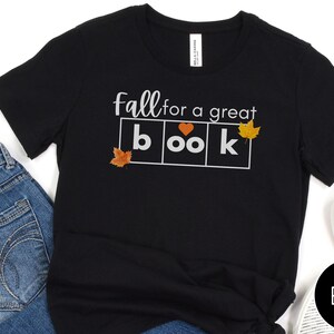 May include: Black t-shirt with the text "fall for a great book" in white letters. The word "book" is in a box with a heart in the "o" and a leaf in each corner of the box.