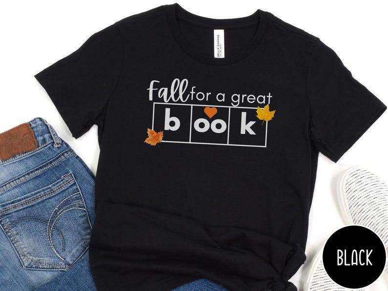 May include: Black t-shirt with the text "fall for a great book" in white letters. The word "book" is in a box with a heart in the "o" and a leaf in each corner of the box.