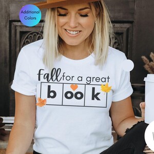 May include: White t-shirt with the text "fall for a great book" in black letters. The word "book" is in individual boxes with a heart in the "oo" box and a small orange leaf in the "k" box.