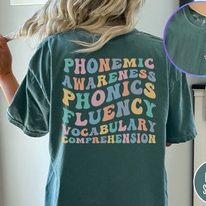 May include: A teal blue t-shirt with the words "phonemic awareness, phonics, fluency, vocabulary, comprehension" printed in rainbow colors on the back. The shirt also has a small graphic of a book with the text "Reading is a right" on the right side of the back.