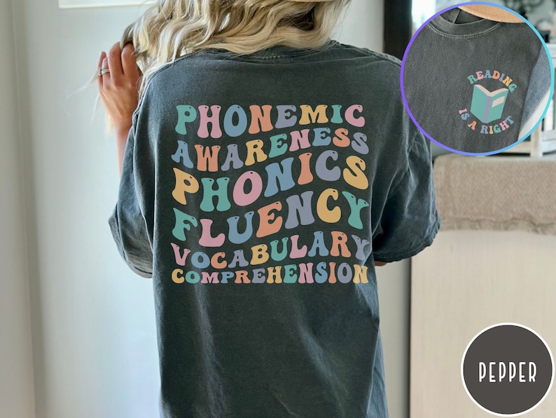 May include: A dark gray t-shirt with the words "phonemic awareness, phonics, fluency, vocabulary, comprehension" printed in rainbow colors on the back. The front of the shirt has a small graphic of a book with the text "Reading is a right" printed around it.