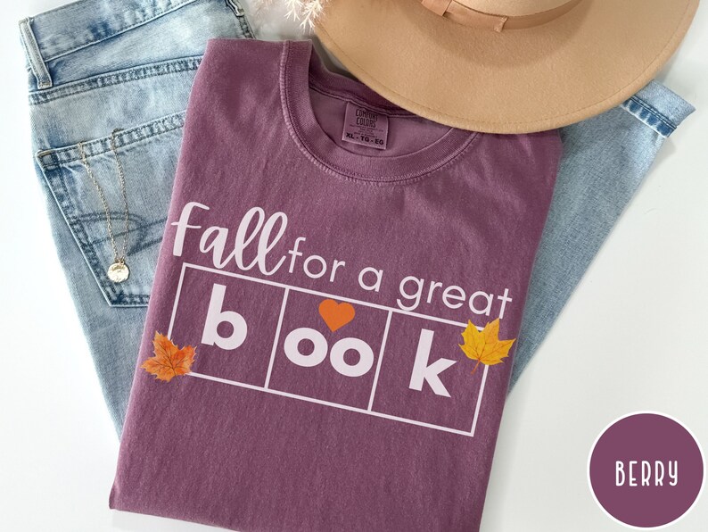 Puede incluir: Una camiseta color granate con el texto "Fall for a great book" en blanco. La palabra "book" est&aacute; en cuadros blancos con un coraz&oacute;n y hojas de oto&ntilde;o en cada cuadro.