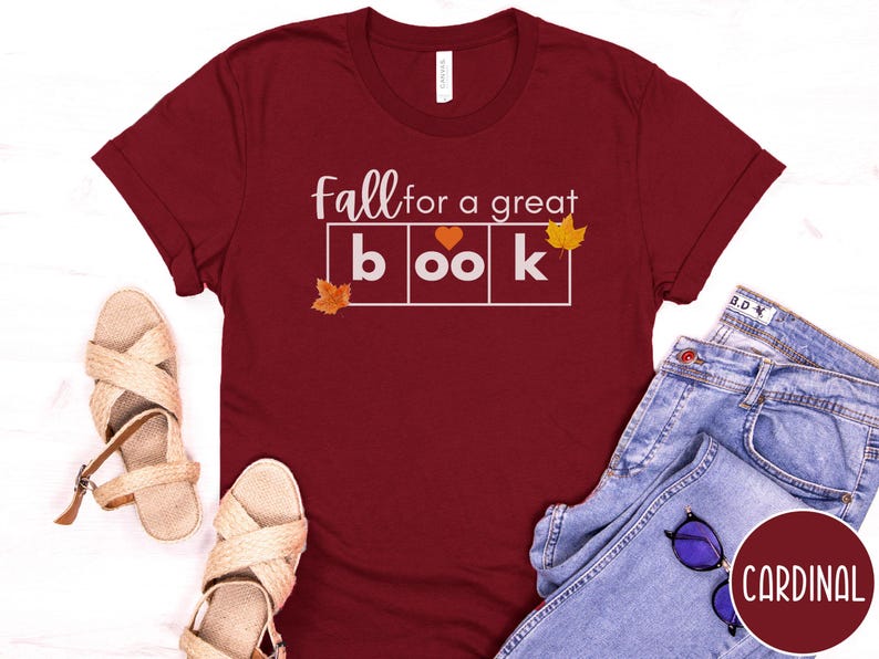 May include: A maroon t-shirt with the text "Fall for a great book" in white letters. The text is in a box with a heart in the middle of the word "book". There are small orange leaf graphics on either side of the text.