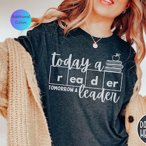 May include: Dark grey heather t-shirt with the text "today a reader tomorrow a leader" in white. The design includes an apple and stack of books. Additional colors are available.