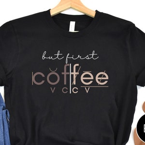 May include: Black t-shirt with the text "but first coffee" in a stylized font with a brown and pink color scheme.